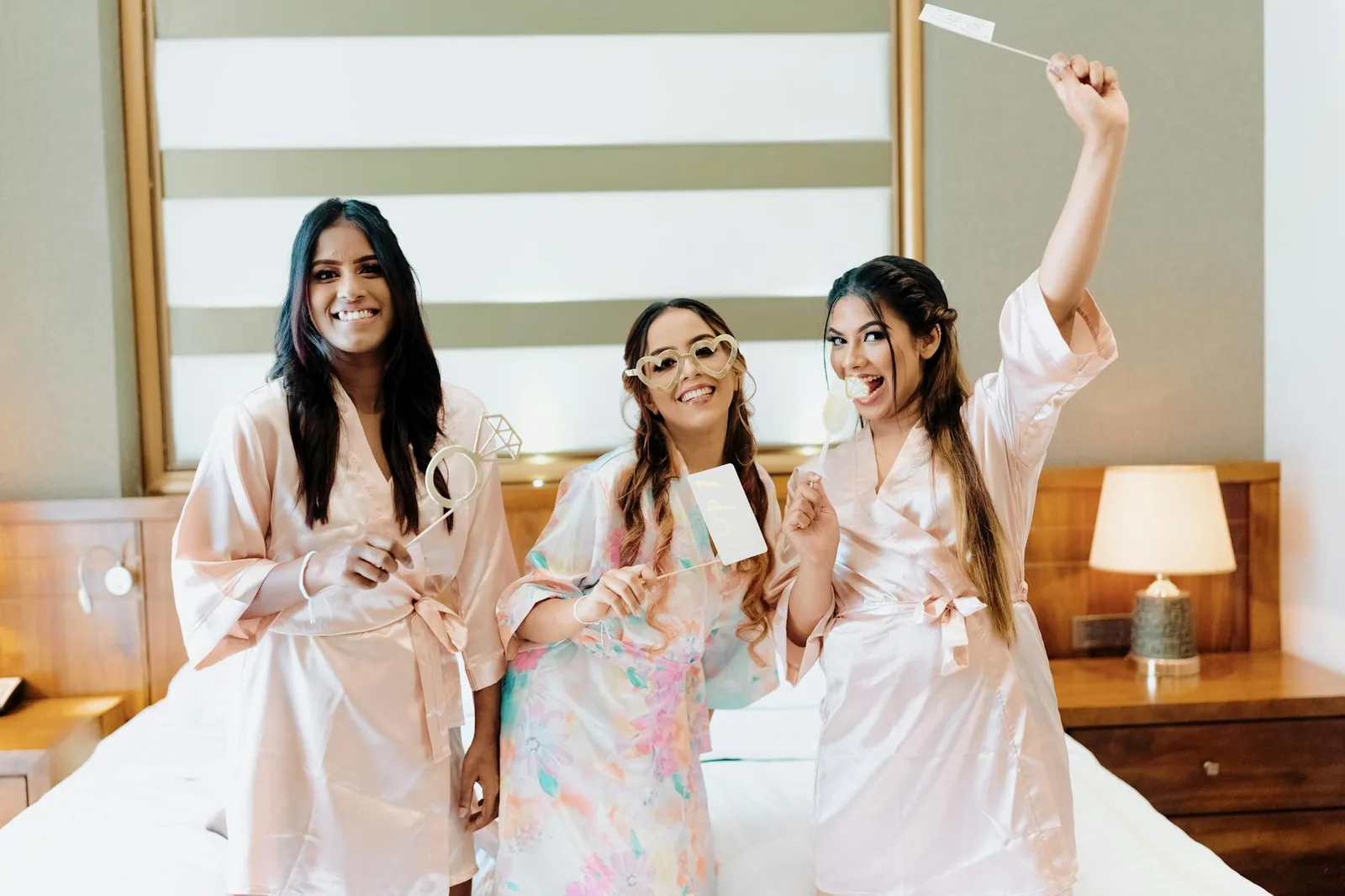Three women in bathrobes enjoying a bridal shower indoors, celebrating with props.