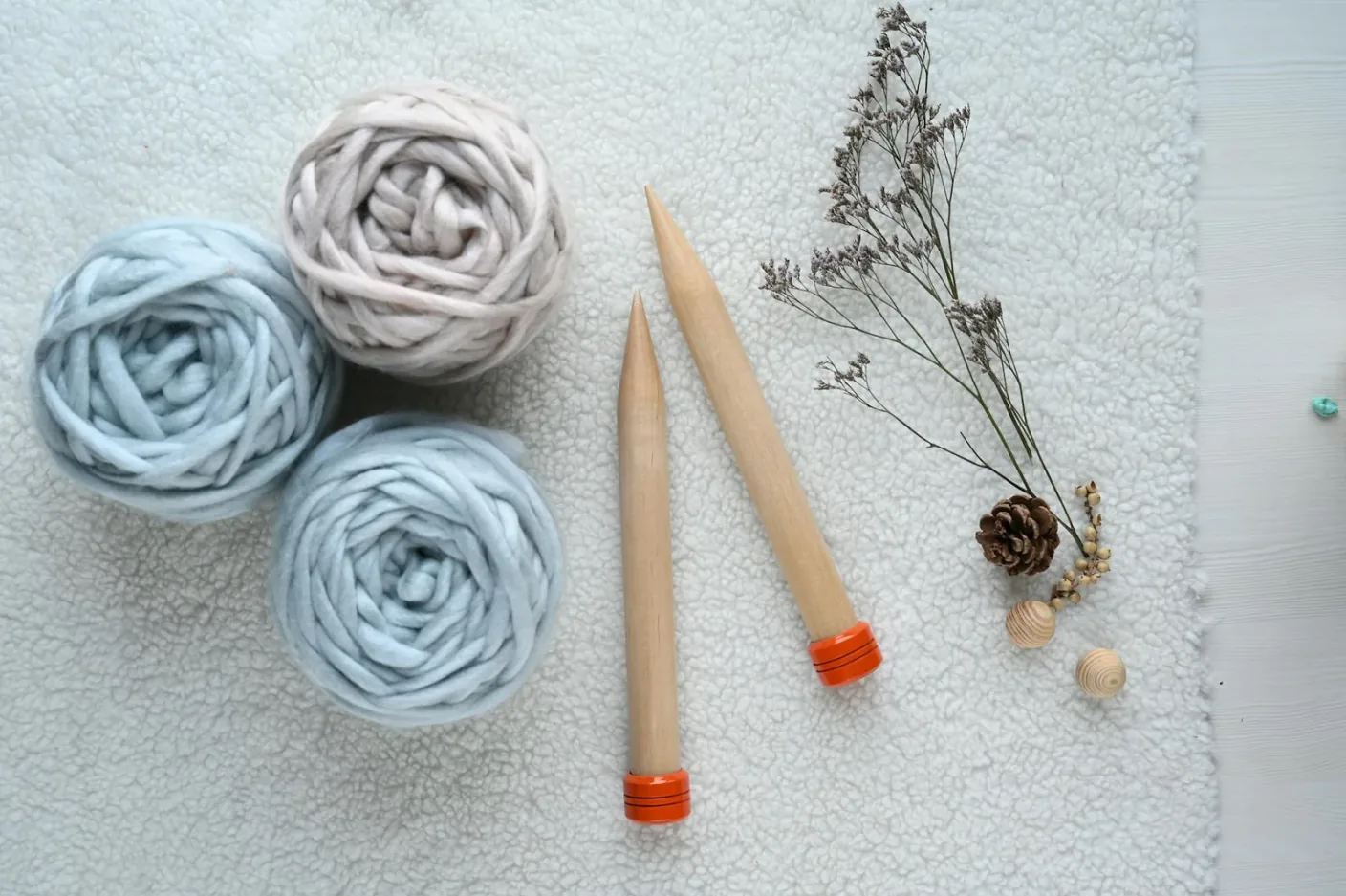A flat lay of knitting supplies including wool yarn balls and needles on a soft surface.