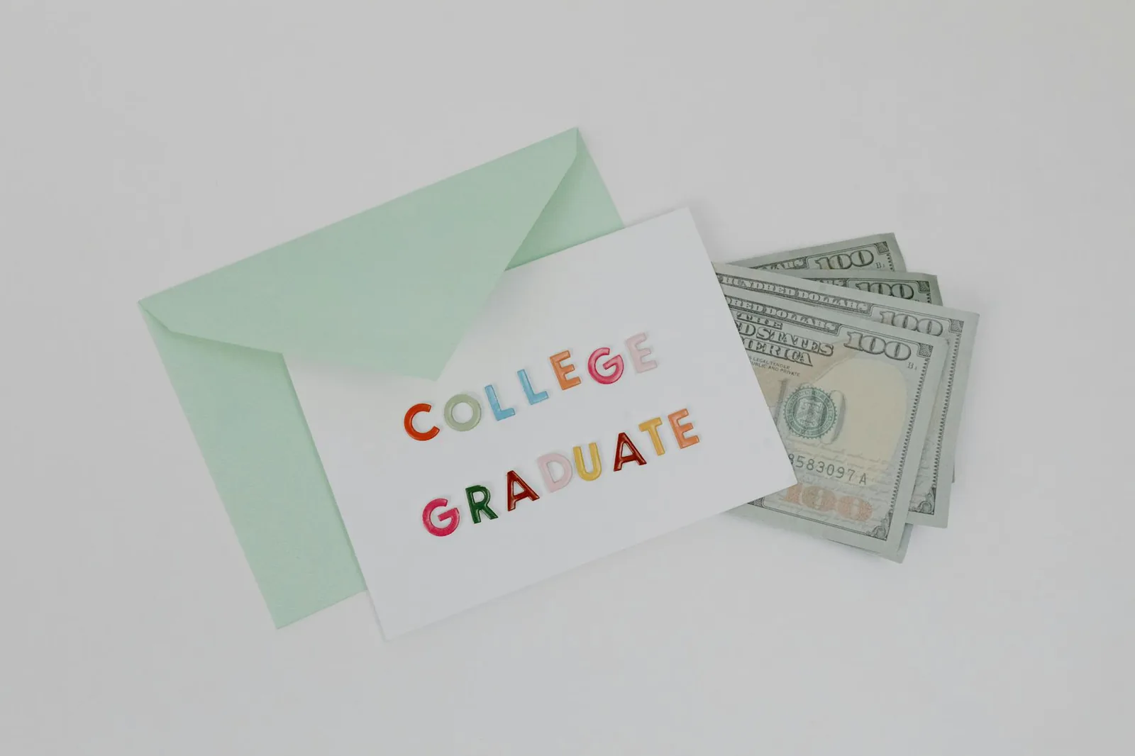 A college graduation card with dollar bills in a mint green envelope on a white surface.