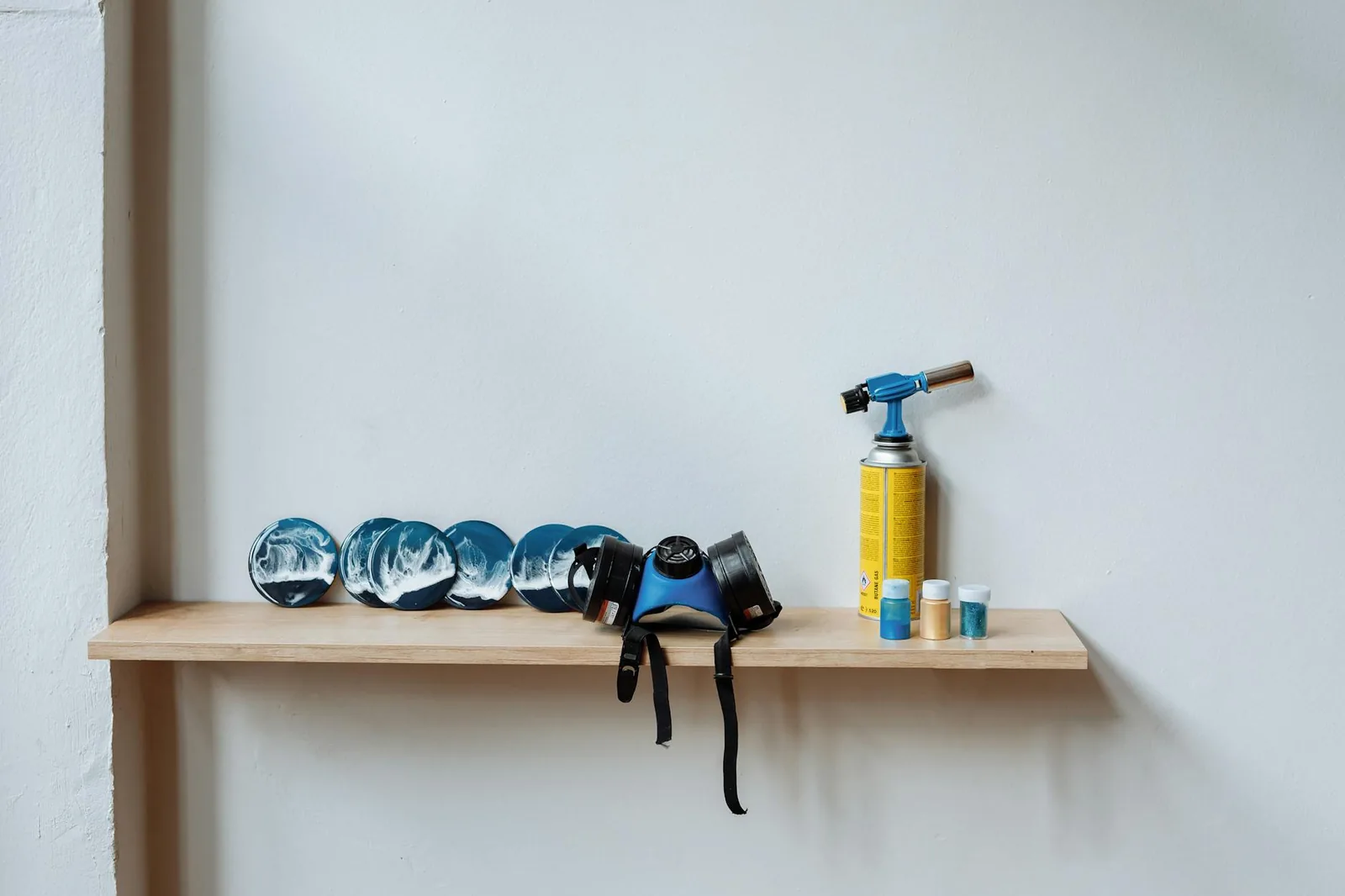 A wooden shelf displaying resin art, blow torch, and safety gear, illustrating a creative workspace.