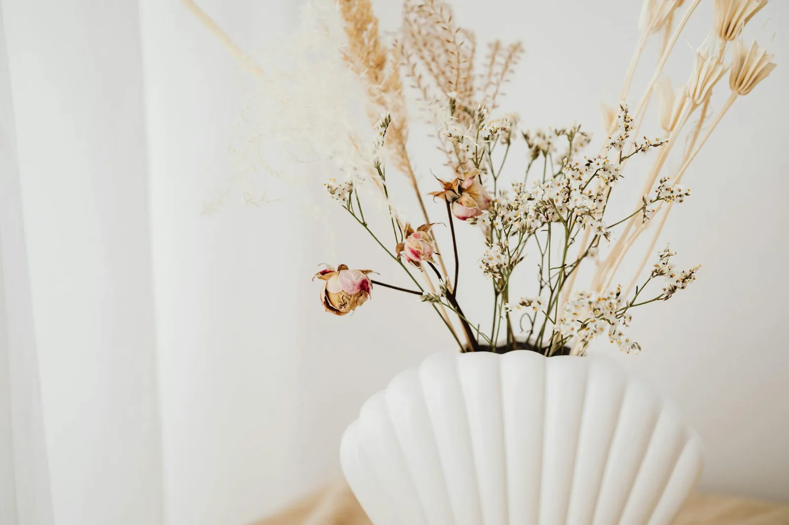 A stylish floral arrangement showcasing dried flowers in a white shell vase, perfect for interior decor.